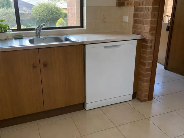 White dishwasher under a kitchen benchtop beside timber cabinets and tiled floor in New Lambton Heights