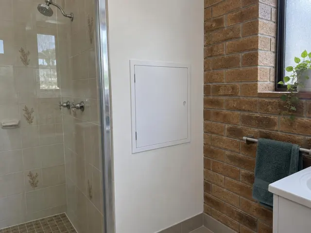 Bathroom wall with a small access panel beside a tiled shower and brick feature wall in Rankin Park