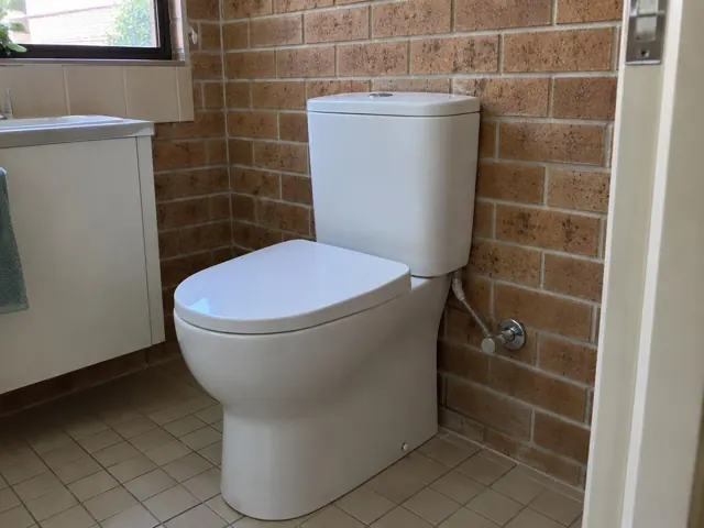 White close-coupled toilet beside brick wall and tiled floor in a bathroom in Elermore Vale